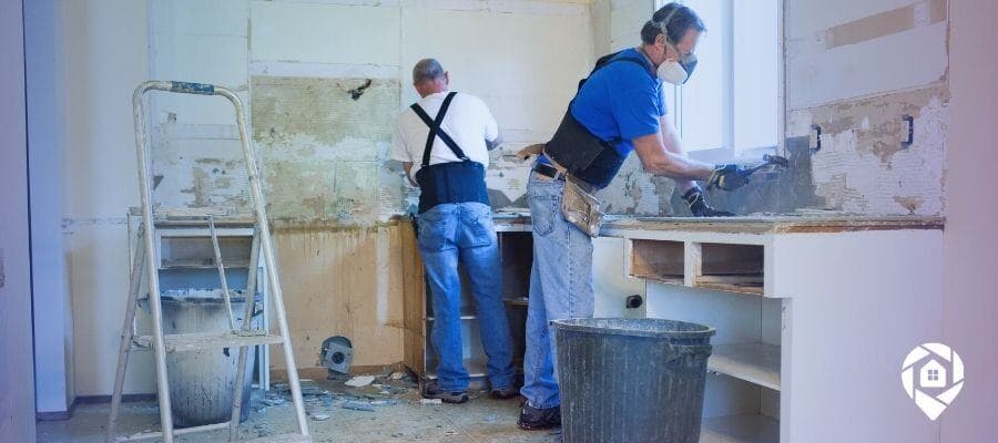 Two contractors renovating a kitchen, removing old cabinets and preparing for upgrades.