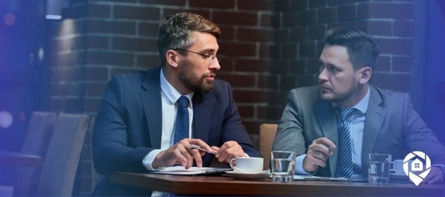 Two real estate investors discussing a wholesale deal strategy over coffee.
