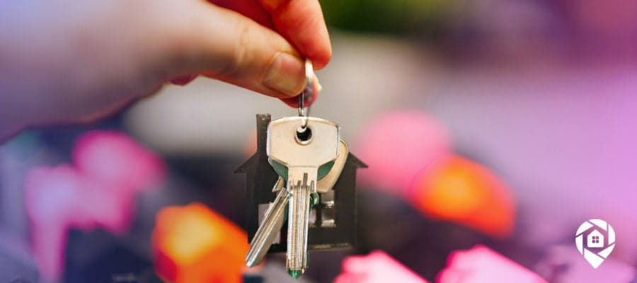 Hands holding keys in front of plastic houses representing real estate investment trusts.