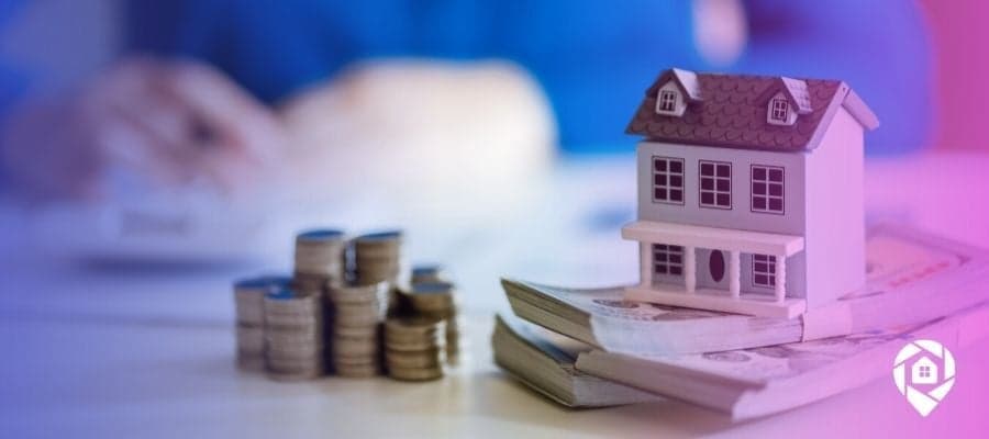 A tiny tax repo house sitting on top of a stack of cash on a desk.