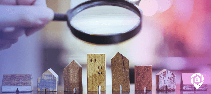 Magnifying glass over wooden houses on a tables searching for how to find homes to flip.
